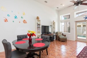 A modern living room with a dining area, a television, and a pool view.