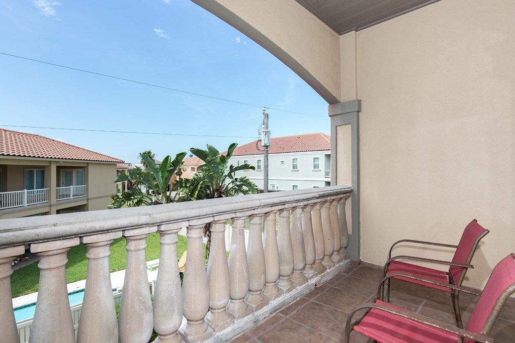 A balcony with a balustrade, a pool, and red chairs.