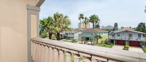 A balcony with a beige railing overlooking a residential area with houses, palm trees, and a clear sky.