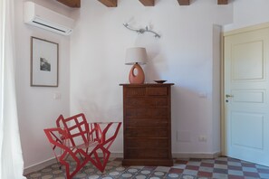 Une pièce comprenant une commode en bois, une chaise rouge, une lampe fixée au mur et une porte.