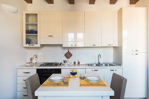 Una cocina moderna con armarios blancos, estufa a gas, pileta y mesa de comedor con platos y vasos.
