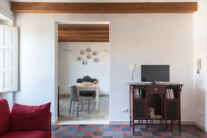 Una sala de estar con un sofá rojo, un televisor sobre un mueble de madera y una zona de comedor con mesa y sillas.