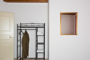 Una habitación con un perchero de metal que sostiene una chaqueta, una puerta blanca y un cuadro en la pared.