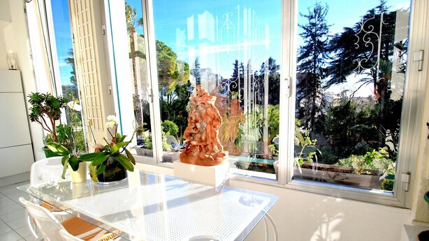 A bright room with a glass table and chairs, a large window with a view of trees and a sculpture. - 4 ROOMS IN THE PALACE OF THE HISTORIC CITY (Cannes)