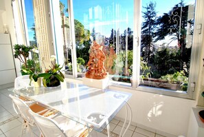 Una habitación luminosa con una mesa y sillas de vidrio, un amplio ventanal con vistas a árboles y una escultura.