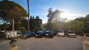 A parking area with several cars and a service vehicle, surrounded by trees and greenery. - 4 ROOMS IN THE PALACE OF THE HISTORIC CITY (Cannes)