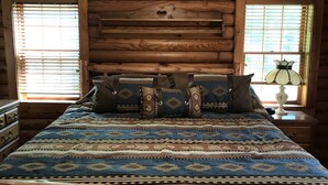 Une chambre à coucher dans un chalet en rondins, avec un lit, des oreillers et une table de chevet avec une lampe.