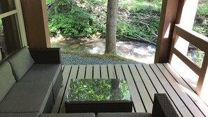 Un espace extérieur abrité, aménagé avec des sièges, offrant une vue sur un ruisseau et la végétation environnante.