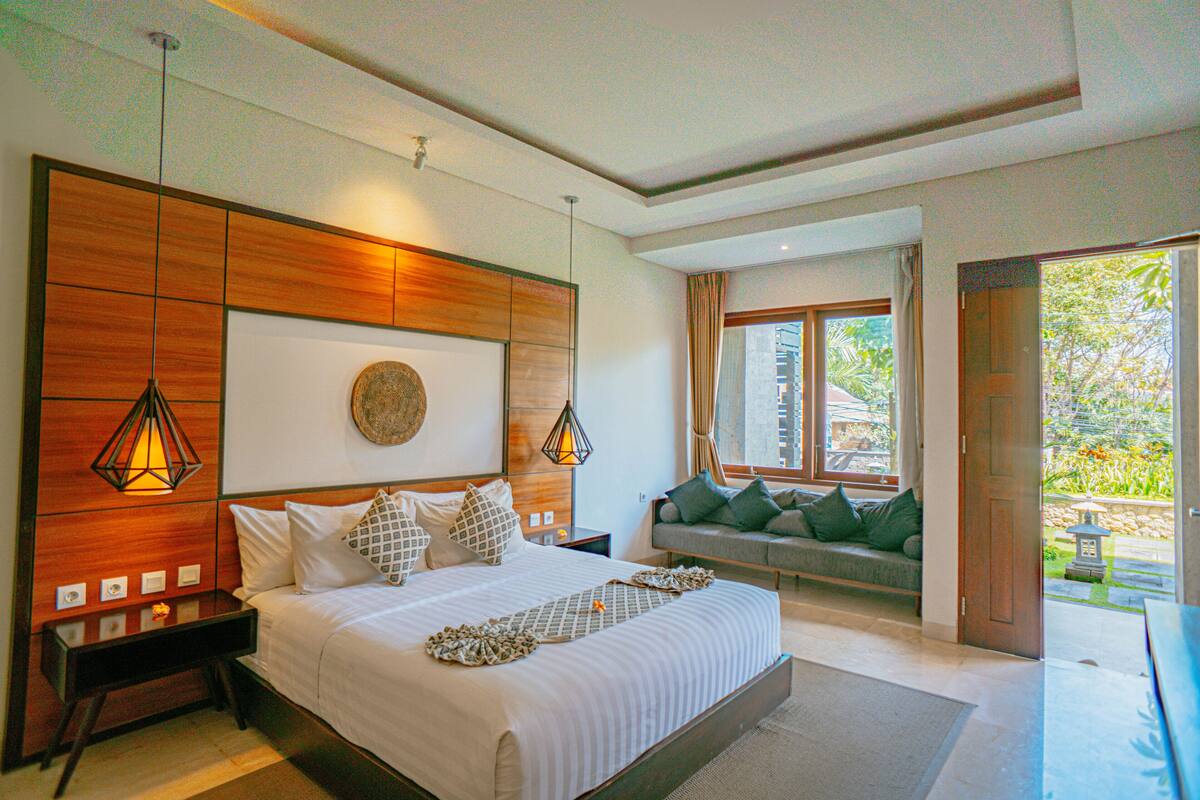 A bedroom with a large bed, bedside tables, a wooden headboard, and a view of the outdoors.