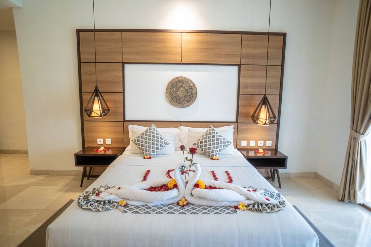 A neatly made bed with a decorative swan towel arrangement, a wooden headboard with a framed artwork, and bedside lamps.