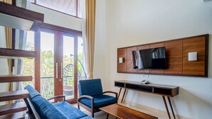 Un salon moderne comprenant un canapé, un fauteuil, une table basse et un téléviseur fixé sur un mur recouvert de panneaux en bois.