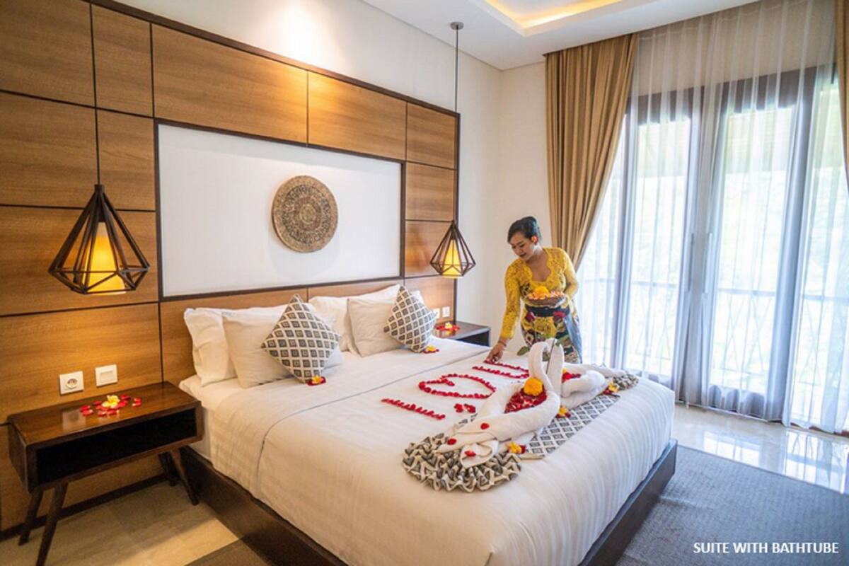 A hotel room with a large bed, a bedside table, a wall-mounted artwork, and a window with curtains.