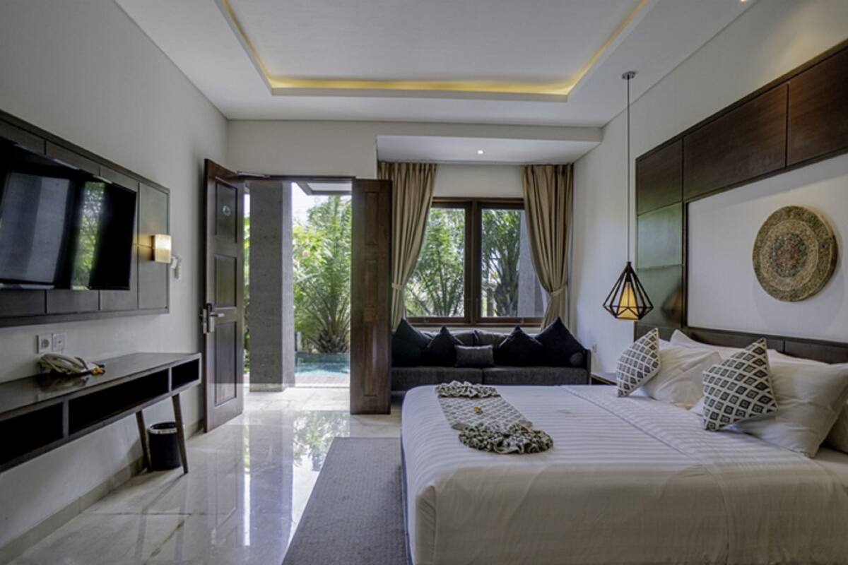 A modern bedroom with a large bed, a TV mounted on the wall, and a view of the outdoors through a door.