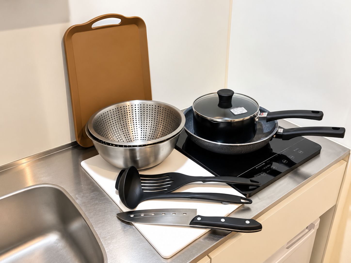 A kitchen counter with a colander, a pot, a spatula, a knife, and a cutting board.