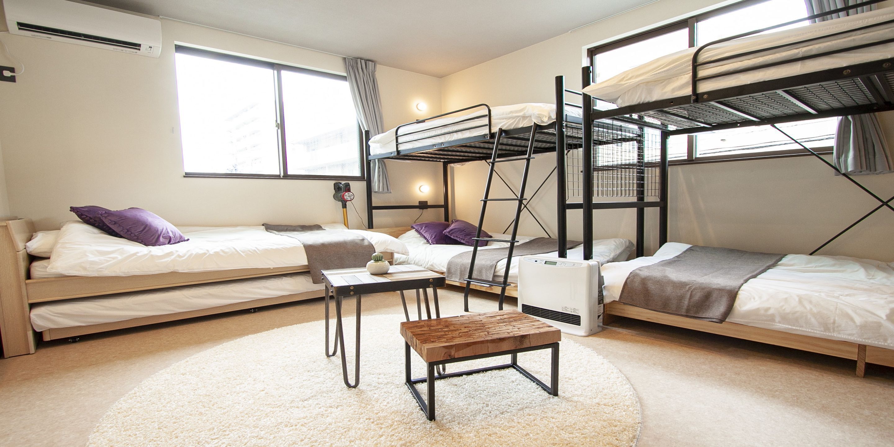 A dormitory room with bunk beds, a desk, a chair, and a small table.