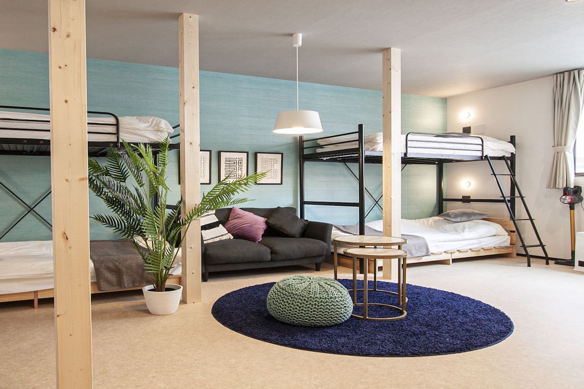 Ein Schlafsaalzimmer mit Etagenbetten, einem kleinen runden Tisch, einem Blumentopf und einem blauen Teppich.