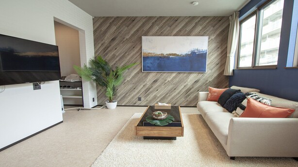 A modern living room with a flat-screen TV, a wooden accent wall, a sofa with cushions, a coffee table, and a potted plant.