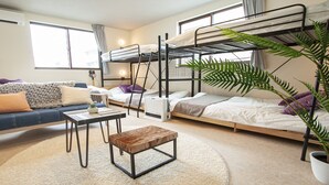 A dormitory room with bunk beds, a sofa, a coffee table, and a potted plant.