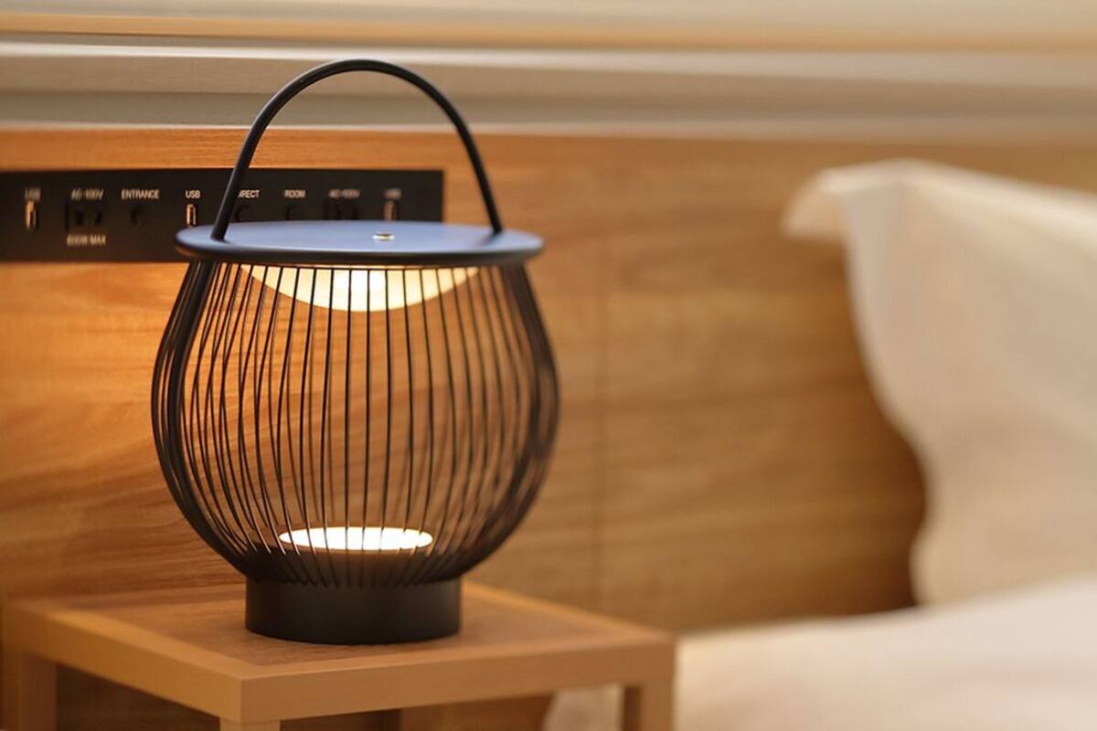 A modern lamp on a bedside table with a wooden headboard and a white pillow.
