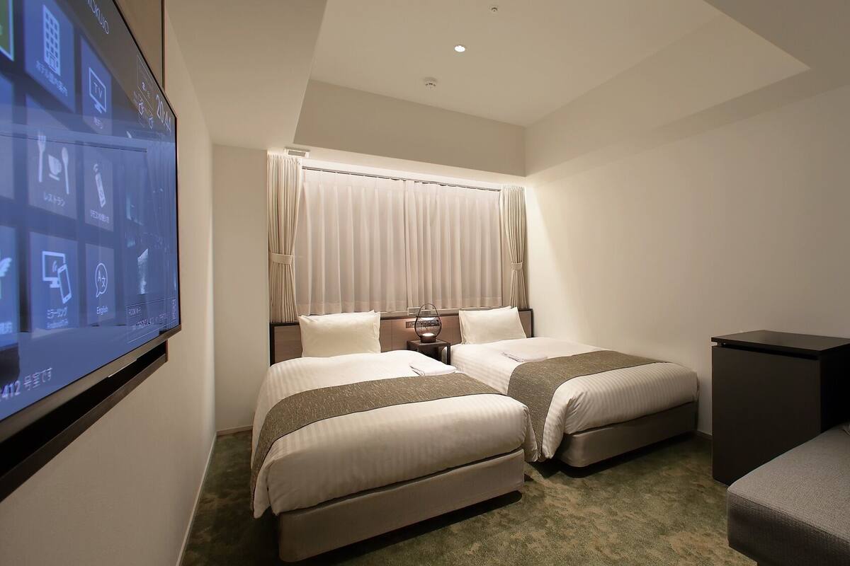 A hotel room with two beds, a TV, a desk, and a chair.