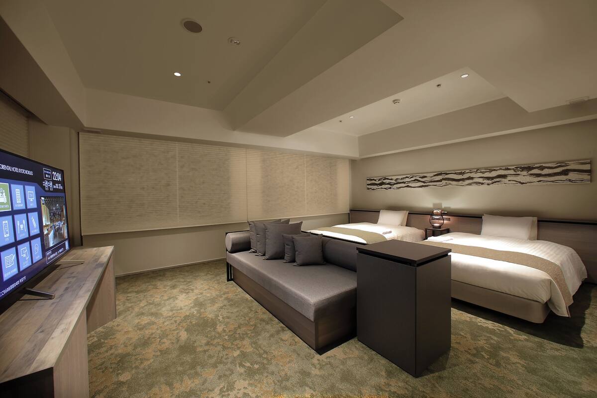 A modern hotel room with a large bed, a sofa, a desk, and a flat-screen TV.