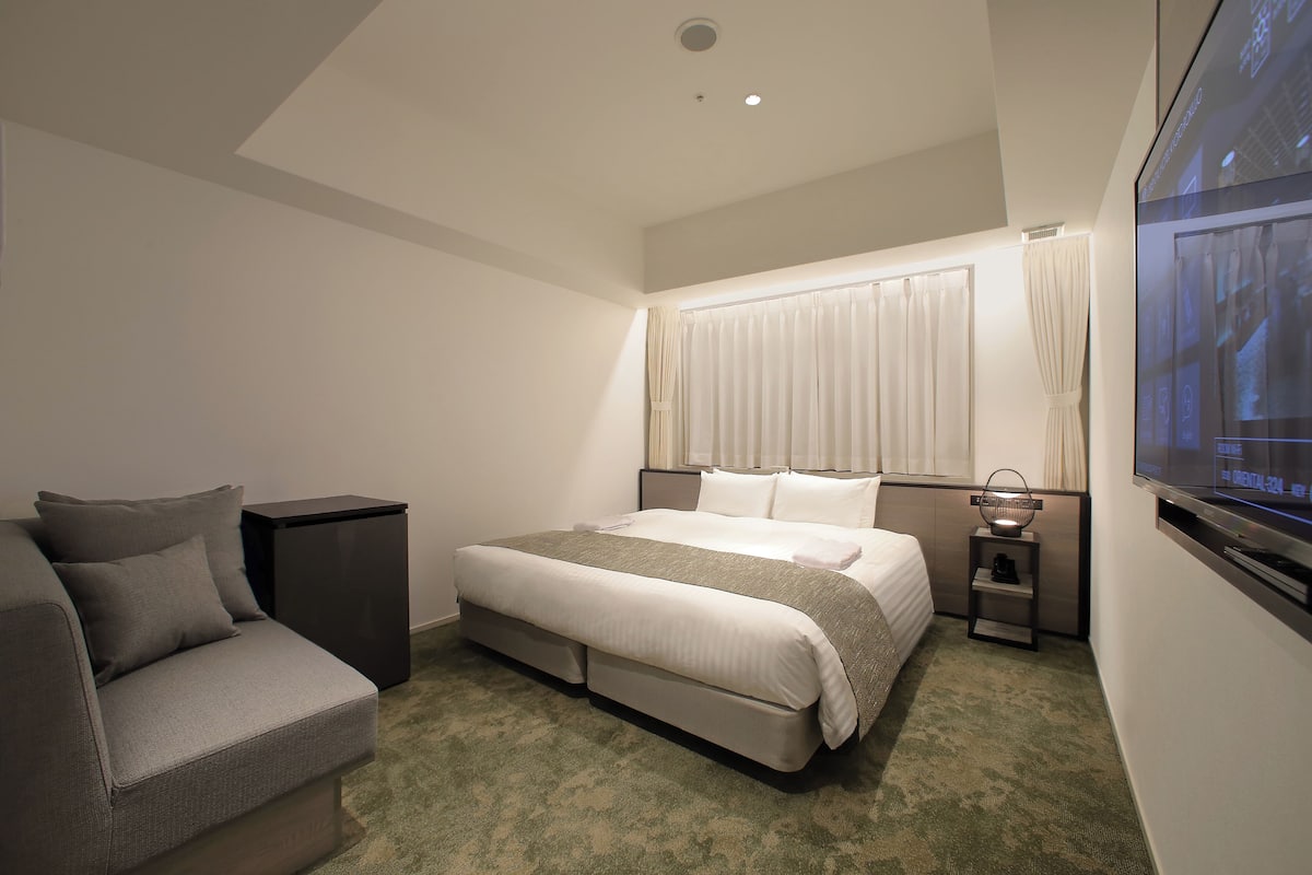 A modern hotel room with a bed, a sofa, a TV, and a small table.