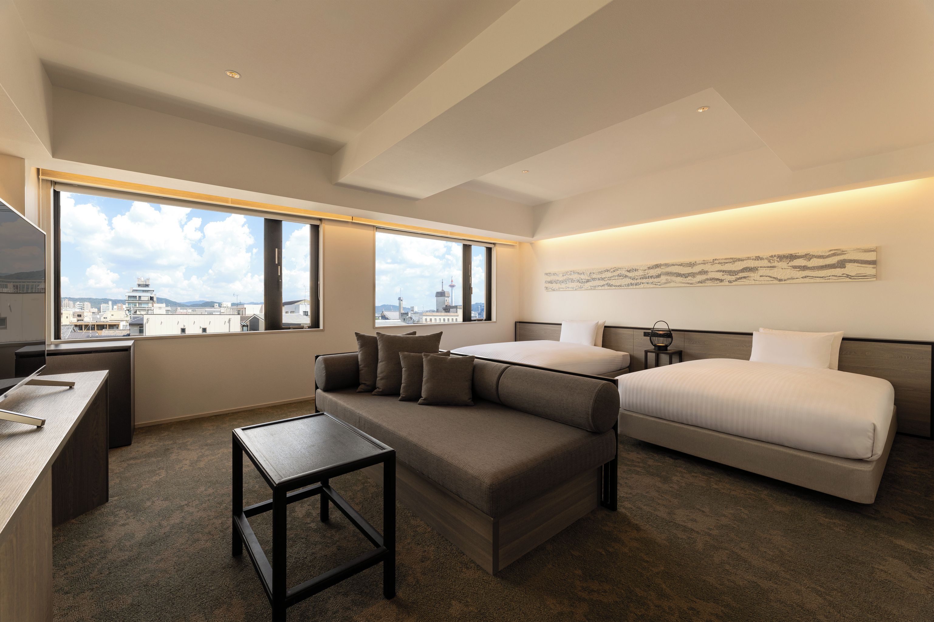Une chambre d’hôtel moderne, dotée d’un grand lit, d’un canapé, d’un bureau et offrant une vue sur le paysage urbain.