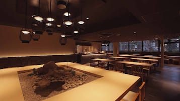 Interior de restaurante con una larga barra, varias mesas y lámparas colgantes.