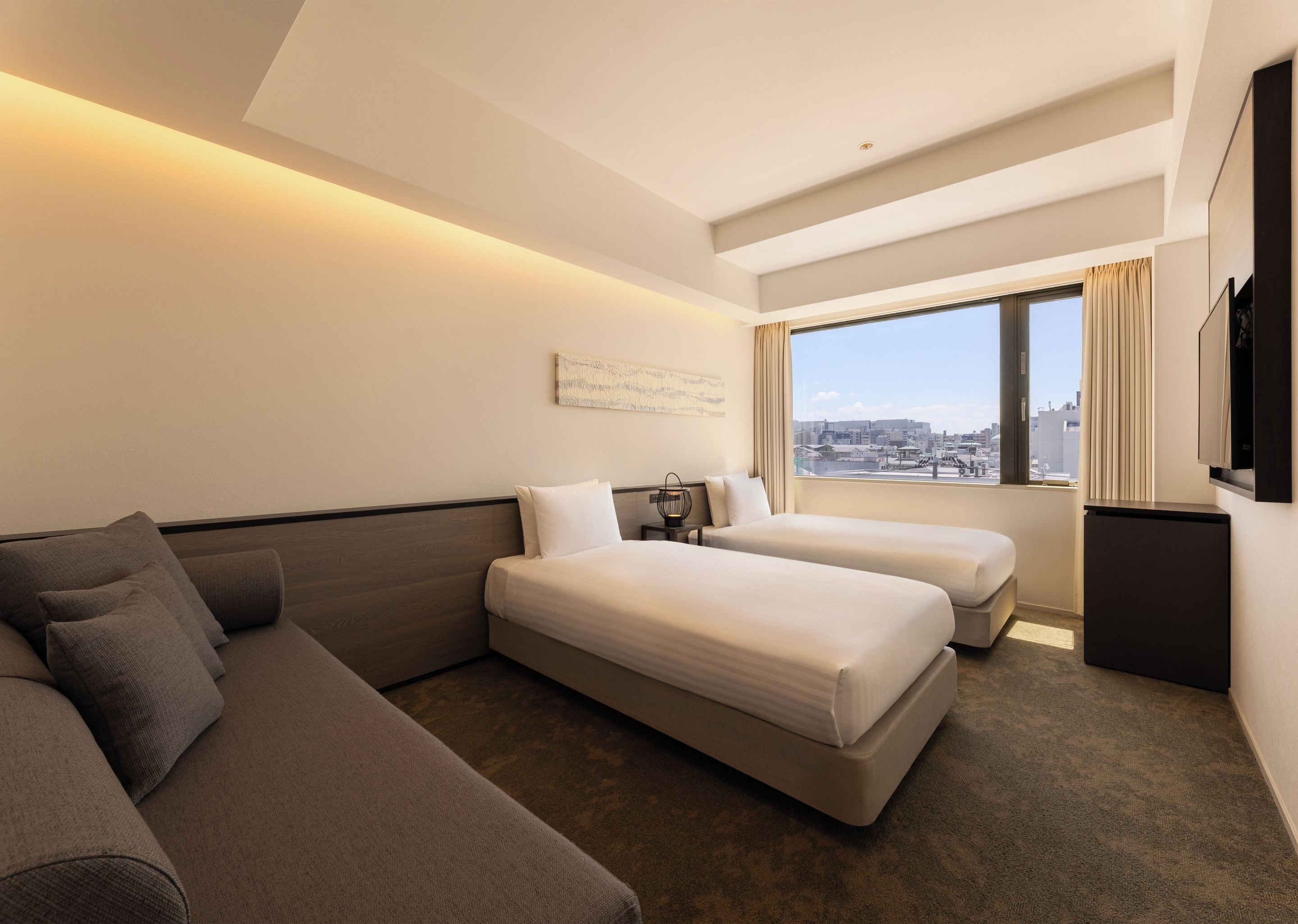 A hotel room with a sofa, two beds, a TV, and a city view.