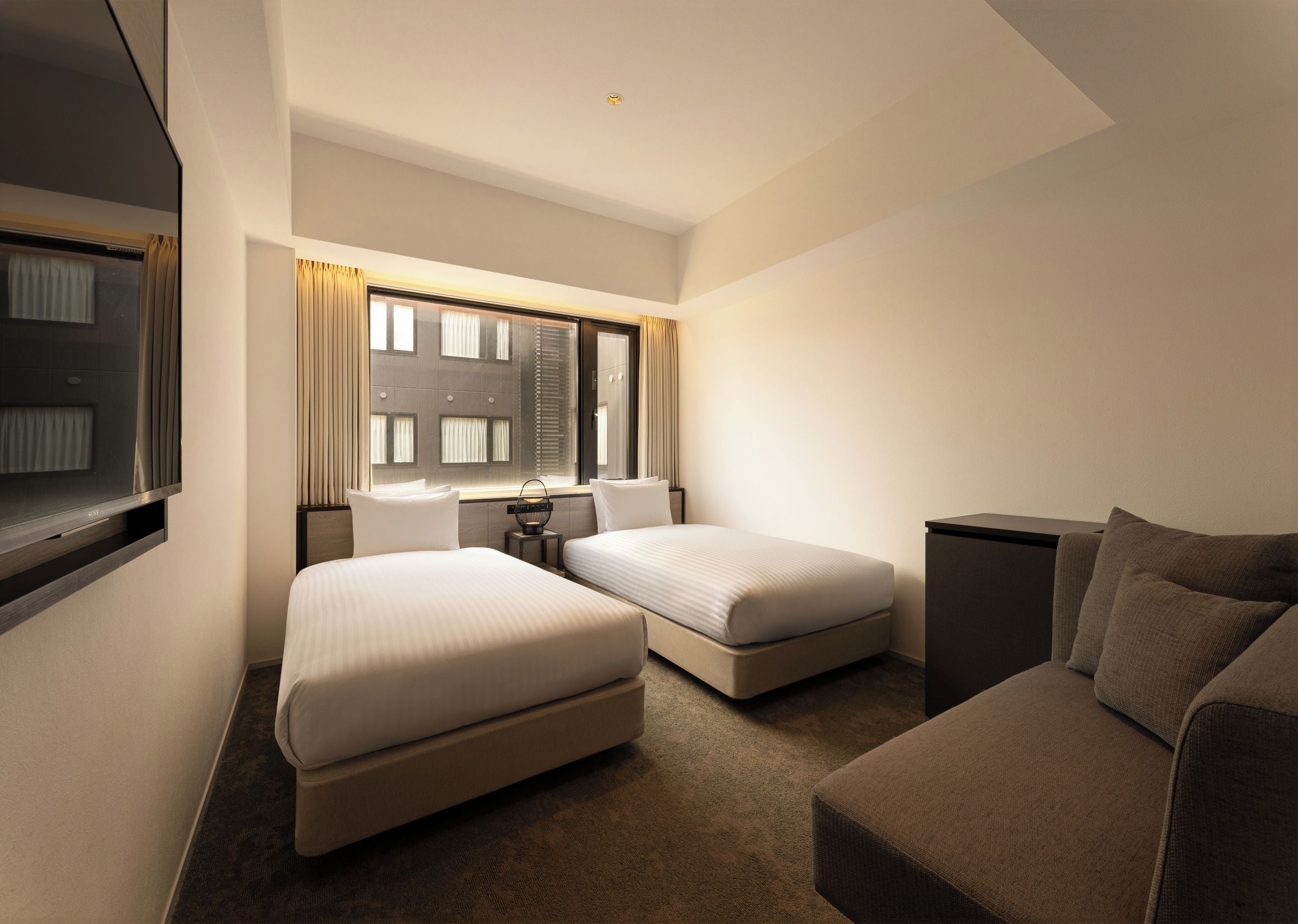 Een hotelkamer met twee bedden, een bank, een televisie en een raam met gordijnen.