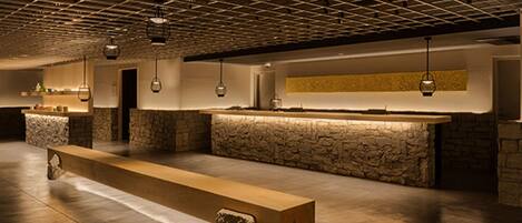 Un'ampia hall con una lunga reception, dettagli in pietra e lampade pendenti.