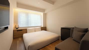 A modern bedroom with a bed, a sofa, a TV, and a window with blinds.