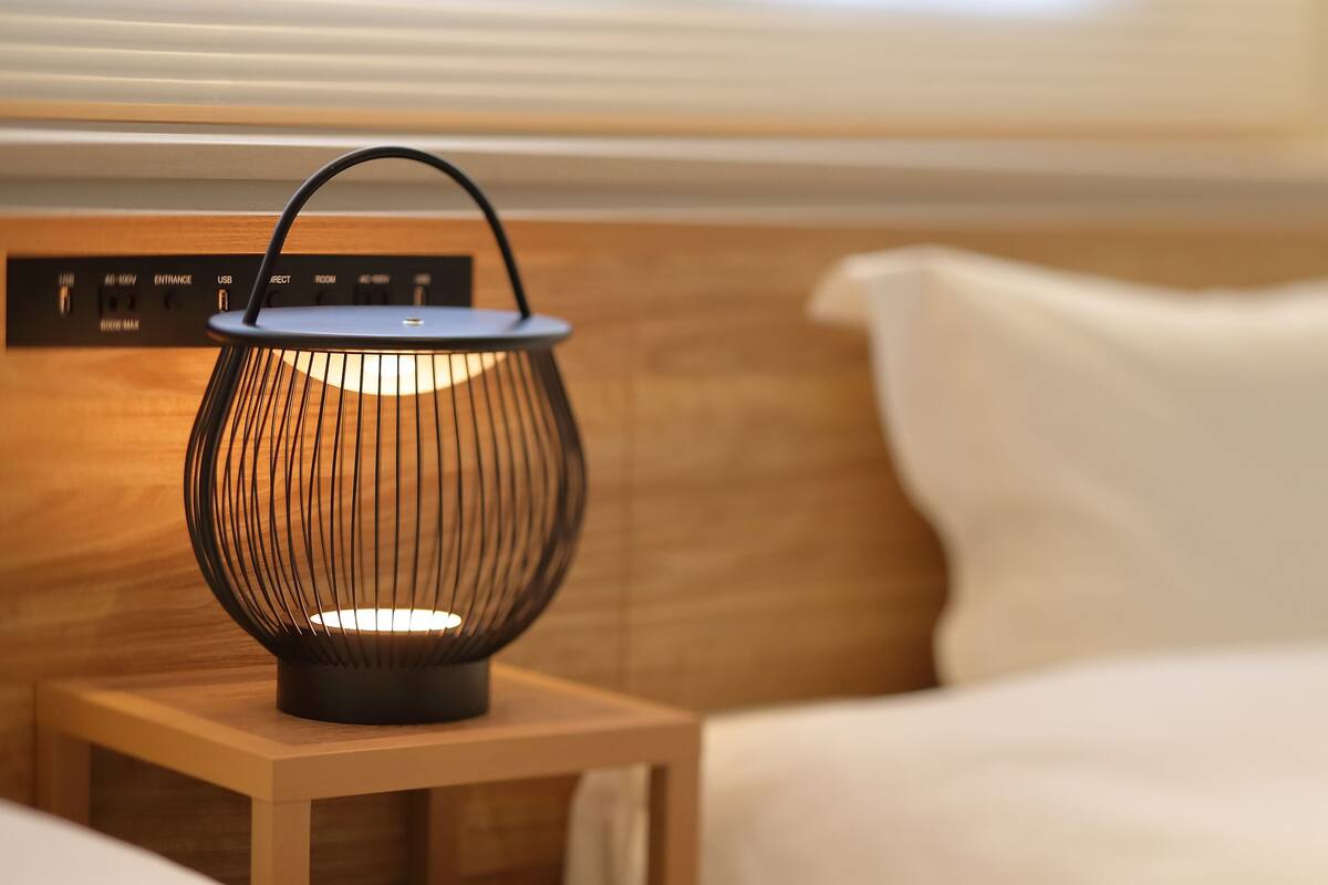 A bedside table with a modern, ribbed lamp and a power strip with multiple outlets.