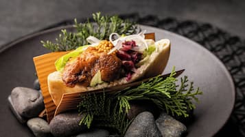 A dish with meat, vegetables, and a bread roll on a dark plate with decorative elements.