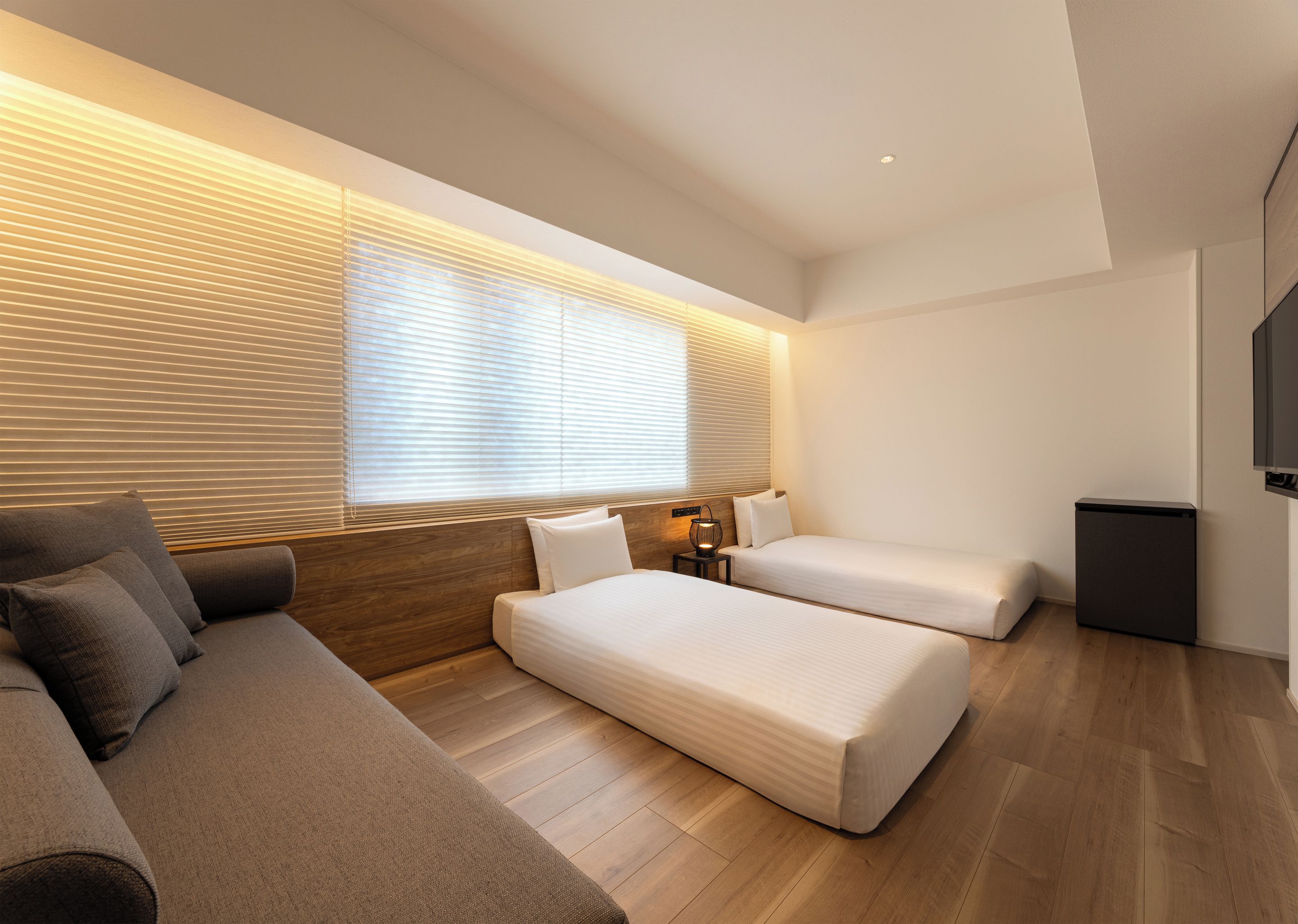 Een moderne hotelkamer met een bank, twee bedden, een kleine tafel met een lamp en een televisie.