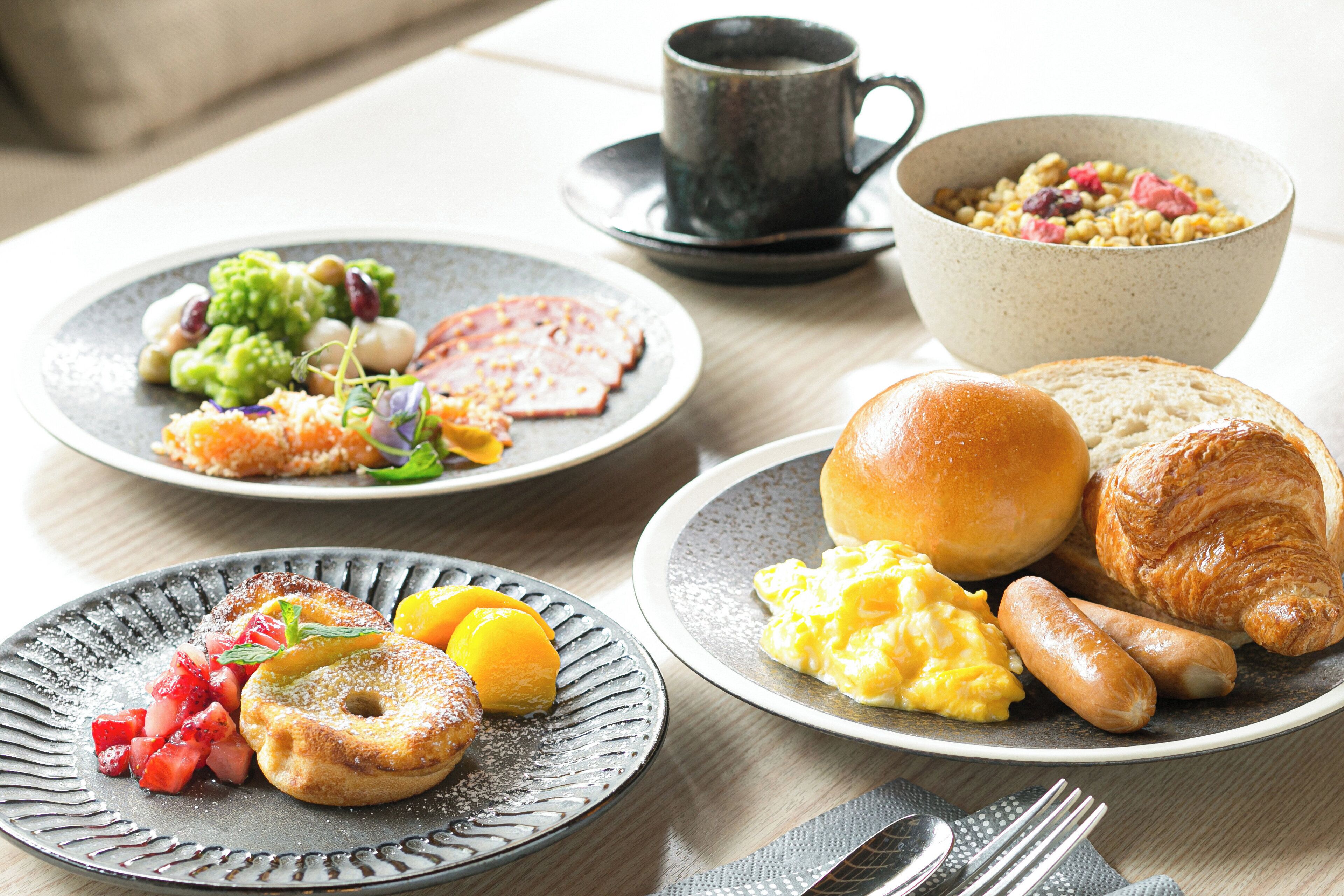 A breakfast table with plates of food, a coffee cup, and a bowl of cereal.