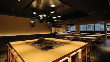 Un restaurante con una larga mesa común rodeada de sillas, una pared de piedra y lámparas colgantes.