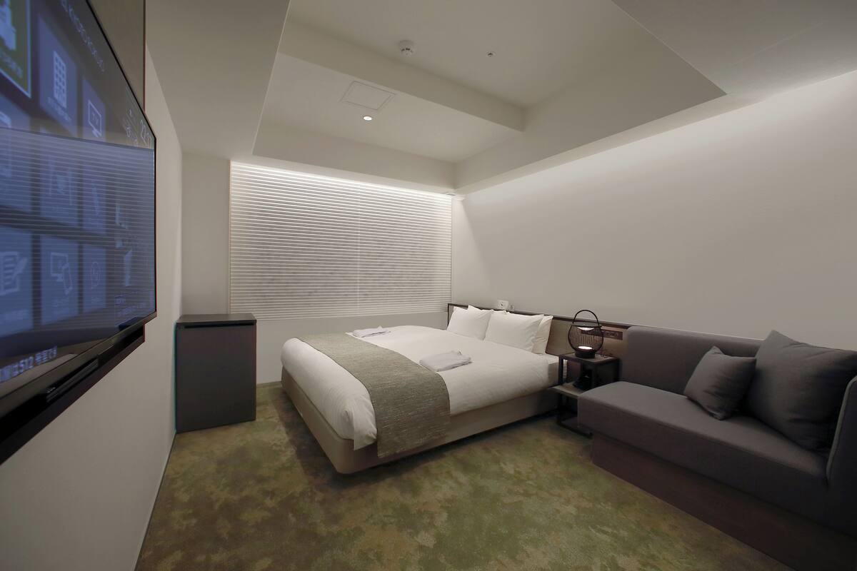 A modern hotel room with a large bed, a sofa, a TV, and a projector screen.