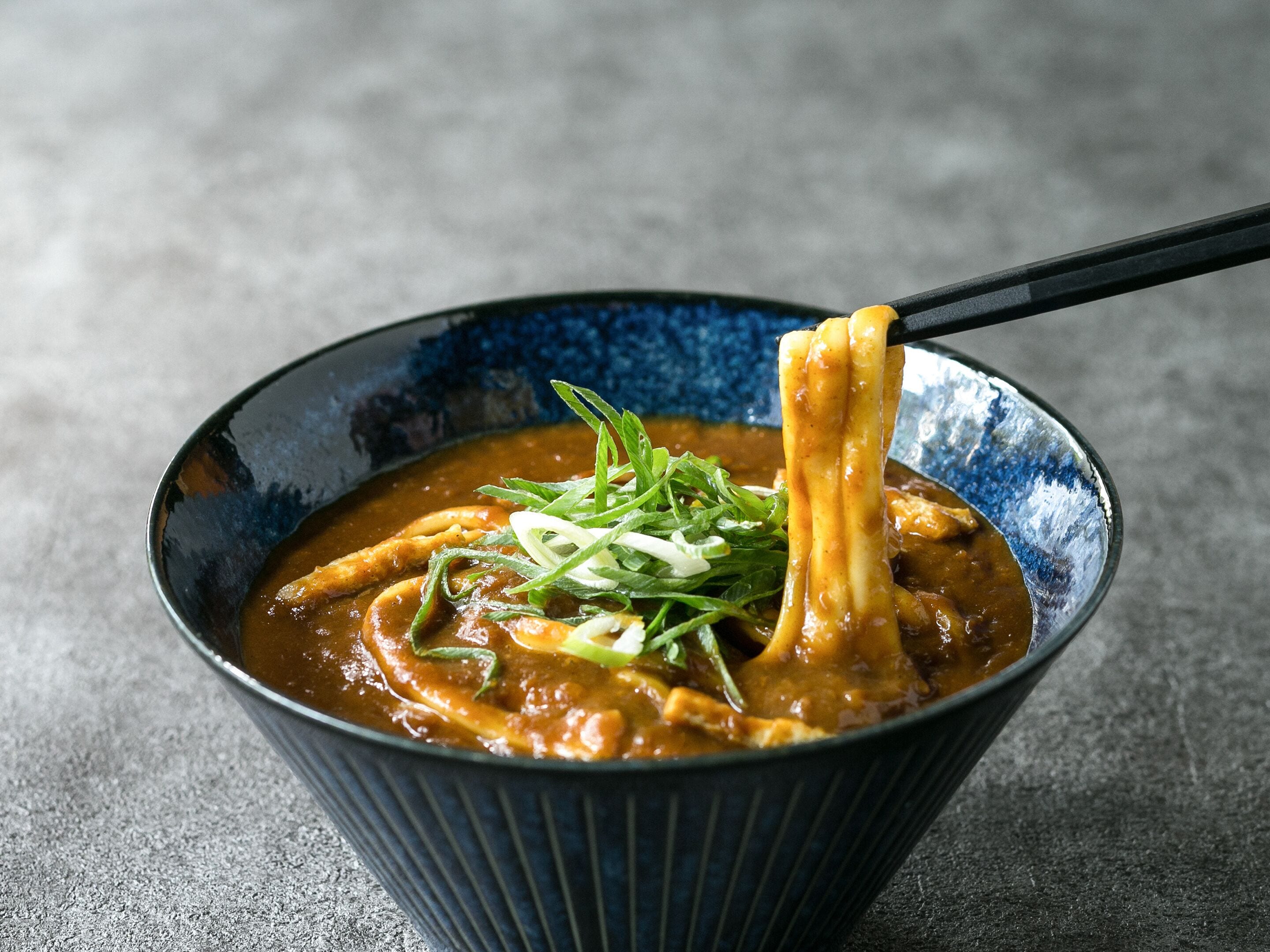 Un plato de ramen con un palillo negro levantando fideos.