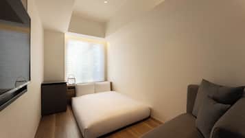 Une chambre à coucher de taille modeste, comprenant un lit simple, une petite table de chevet, une chaise et une fenêtre avec des stores.