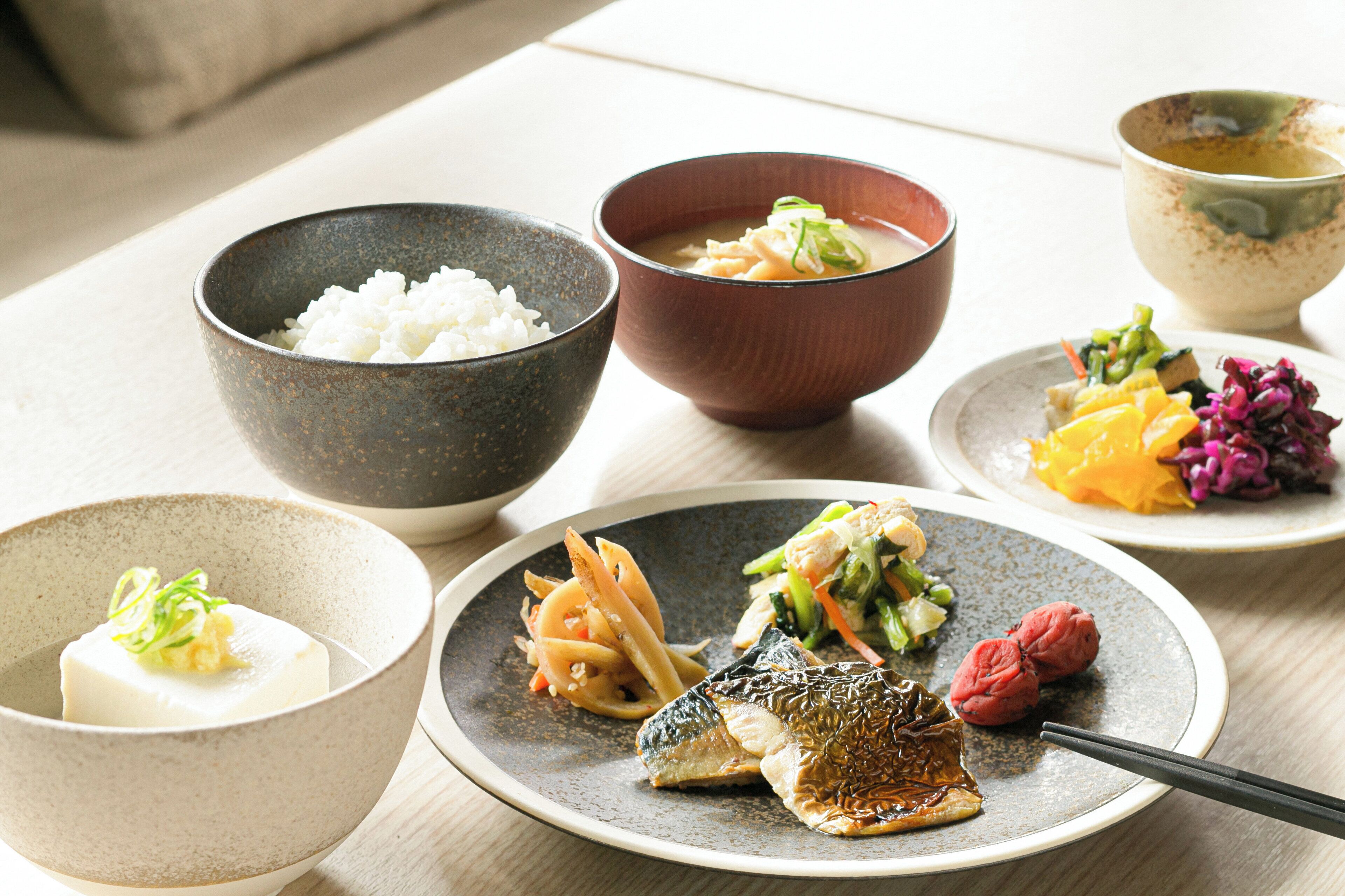 Una mesa con varios platos que incluyen arroz, sopa, pescado y verduras.