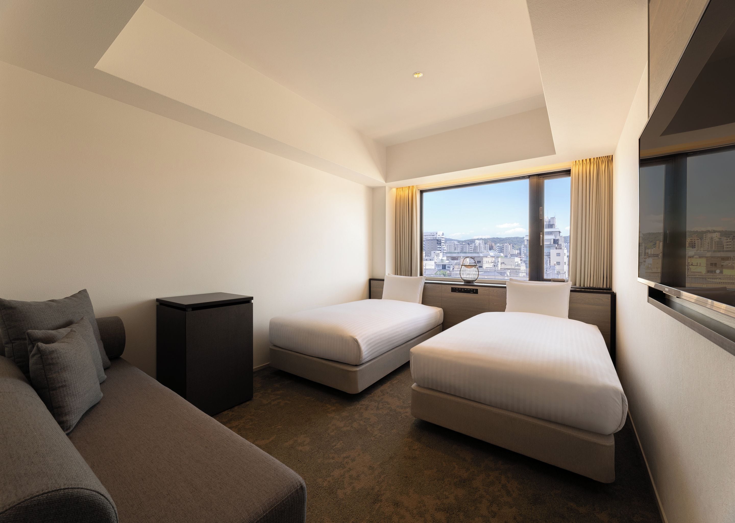 Une chambre d’hôtel avec un canapé, deux lits simples, une petite table, une télévision et une vue sur la ville.