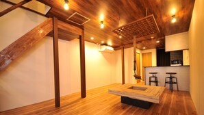 Un intérieur moderne avec un plancher en bois, des poutres apparentes, une table centrale et un coin cuisine équipé de tabourets.