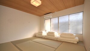 Une pièce avec des tatamis, un futon, une porte coulissante en verre et un appareil de climatisation.