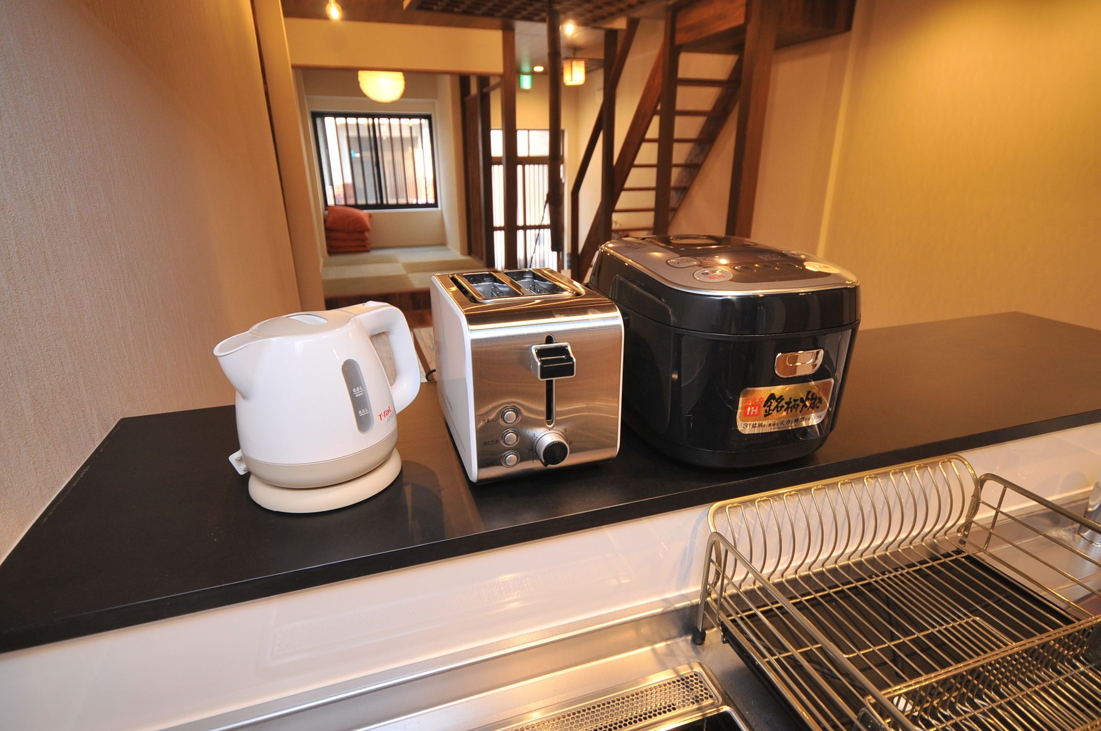 Una kitchenette con cafetera, tostadora y un recipiente negro, probablemente para guardar objetos.