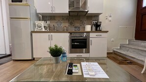 A modern kitchen with white cabinets, a built-in oven, a microwave, and a glass-top table with a remote control and a plant. - (0Β) Two Bedroom Ground Floor PRIVATE Apartment in Psiri-Historic Center! (Athina)