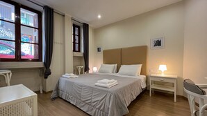 A hotel room with a large bed, two bedside tables, a chair, a small table, and a window with curtains. - (0Β) Two Bedroom Ground Floor PRIVATE Apartment in Psiri-Historic Center! (Athina)