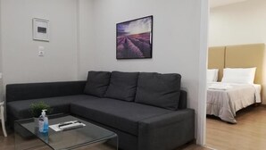 A modern living room with a dark grey sofa, a glass coffee table, and a framed picture of lavender fields on the wall. - (0Β) Two Bedroom Ground Floor PRIVATE Apartment in Psiri-Historic Center! (Athina)