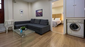 A modern living room with a grey sofa, a glass coffee table, and a washing machine. - (0Β) Two Bedroom Ground Floor PRIVATE Apartment in Psiri-Historic Center! (Athina)