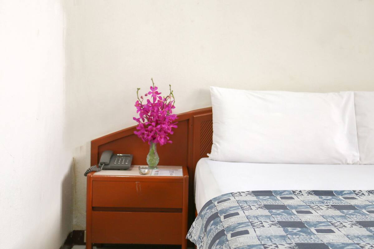 A hotel room with a bed, a nightstand with a phone, and a vase with flowers.